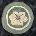 Decorative wooden coaster with floral design on a dark fabric background